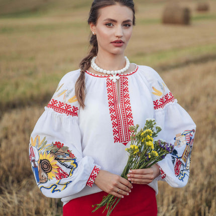 Woman in traditional embroidered blouse and red pants holding flowers in a field