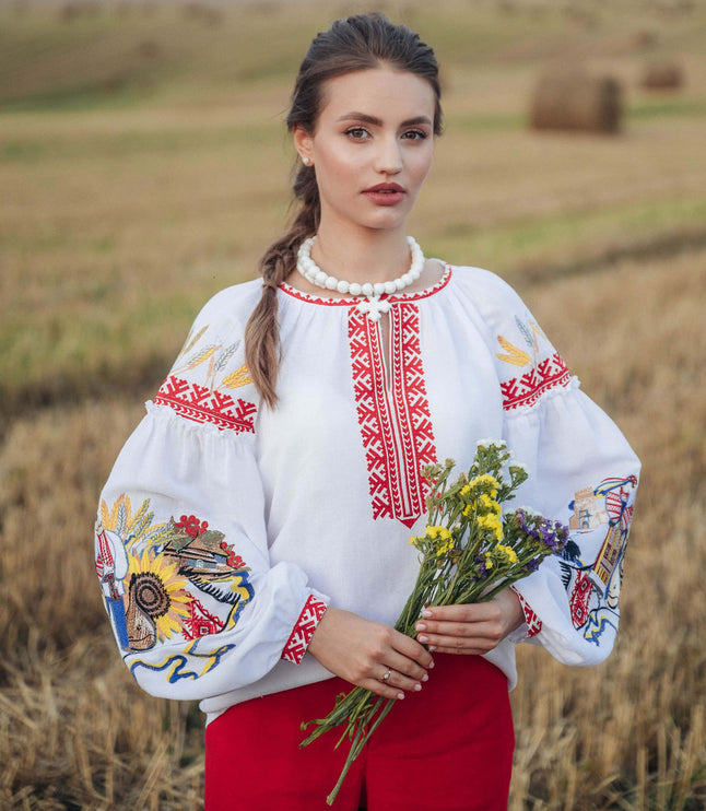 Woman in traditional embroidered blouse and red pants holding flowers in a field